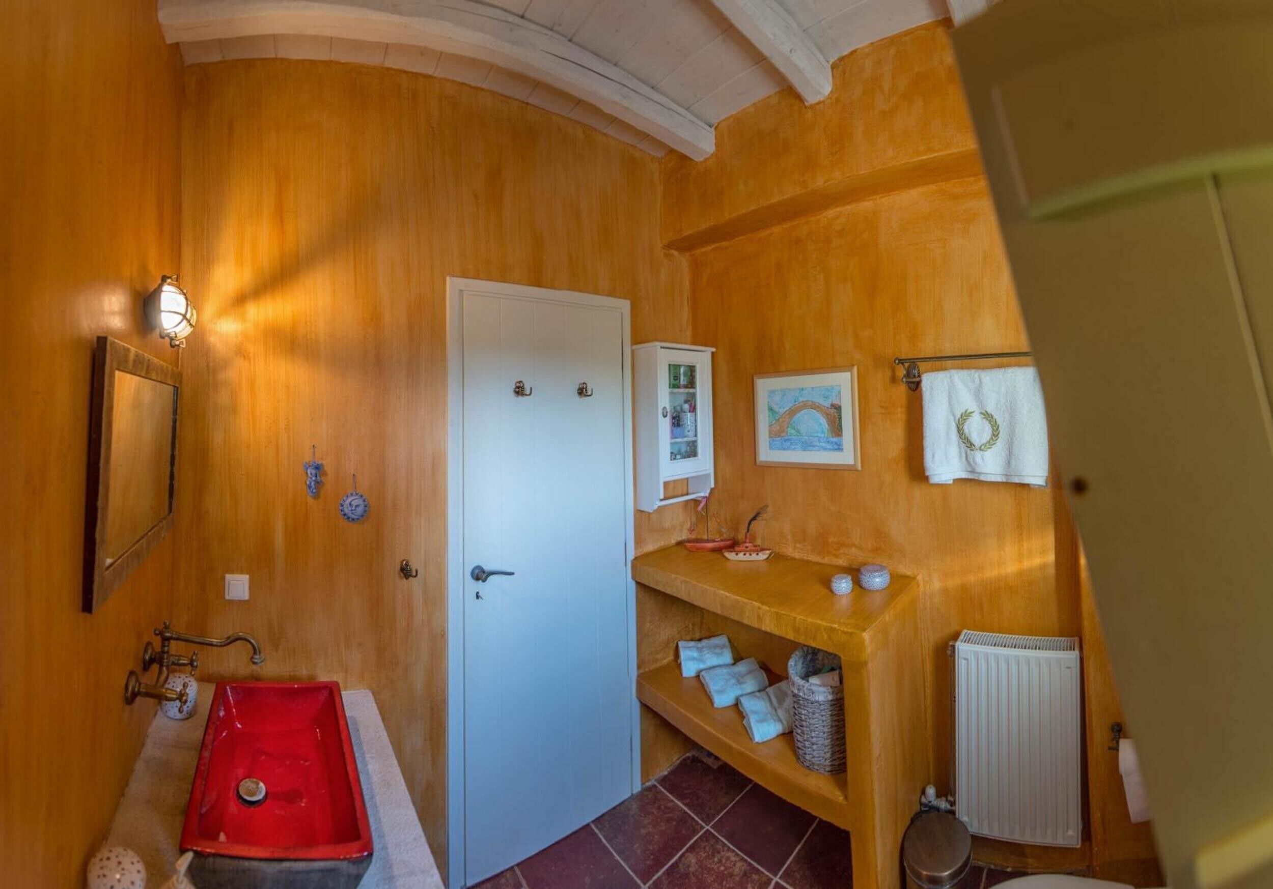 Un baño con un lavamanos rojo, una puerta blanca, un armario blanco, un estante con toallas y un radiador.