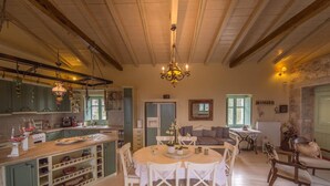 A spacious kitchen with wooden beams, a dining area with white chairs, and a cozy living room with a fireplace.