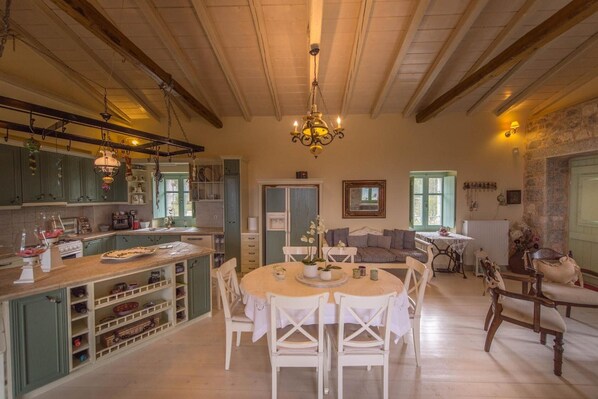 A spacious kitchen with wooden beams, a dining area with white chairs, and a cozy living room with a fireplace.