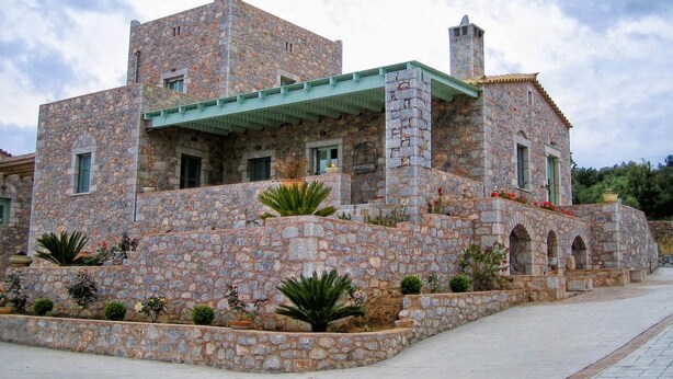 A stone building with multiple levels, a green roof, and a courtyard with plants.