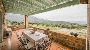 A covered outdoor dining area with a table set for two, stone walls, and a view of the countryside.