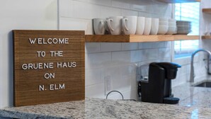 Una cocina con un letrero de madera que dice 'WELCOME TO THE GRUENE HAUS ON N. ELM', una encimera y una cafetera.