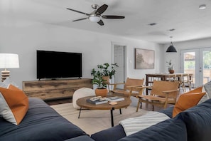 A modern living room with a flat-screen TV, wooden furniture, a ceiling fan, and a dining area with chairs and a table.