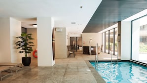 Un área moderna de piscina interior con vista despejada, una planta en maceta y un espacio de descanso con sillas.