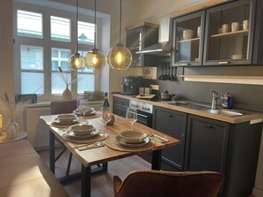 A modern kitchen with a wooden table set for dining, a built-in oven, and a coffee machine. - Cozy and lovingly furnished vacation apartment in the old town of Duderstadt (Duderstadt)