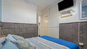 A bedroom with a bed, a TV, a wardrobe, and a stone-patterned wall. - Vacation Apartment 'Casa Lita' with Shared Pool, Private Terrace, and Wi-Fi (Antigua)