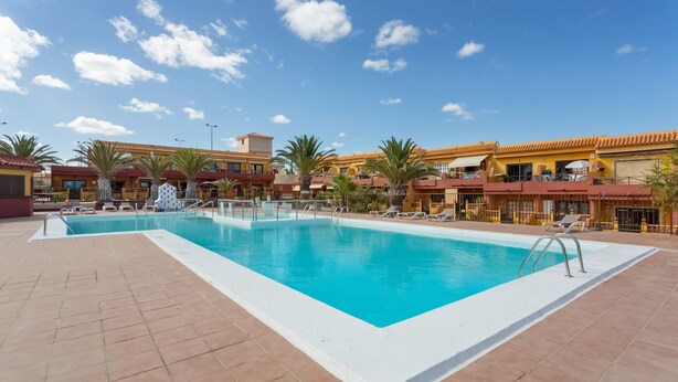 A swimming pool with a tiled deck, palm trees, and buildings with yellow and red roofs. - Vacation Apartment 'Casa Lita' with Shared Pool, Private Terrace, and Wi-Fi (Antigua)