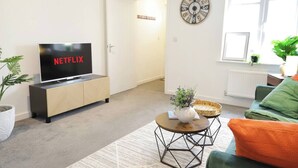 A modern living room with a flat-screen TV on a cabinet, a round coffee table, a green sofa, and a clock on the wall.