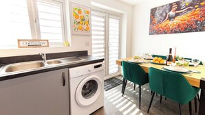 A modern kitchen with a washing machine, a coffee bar sign, and a dining area with a table set for two.