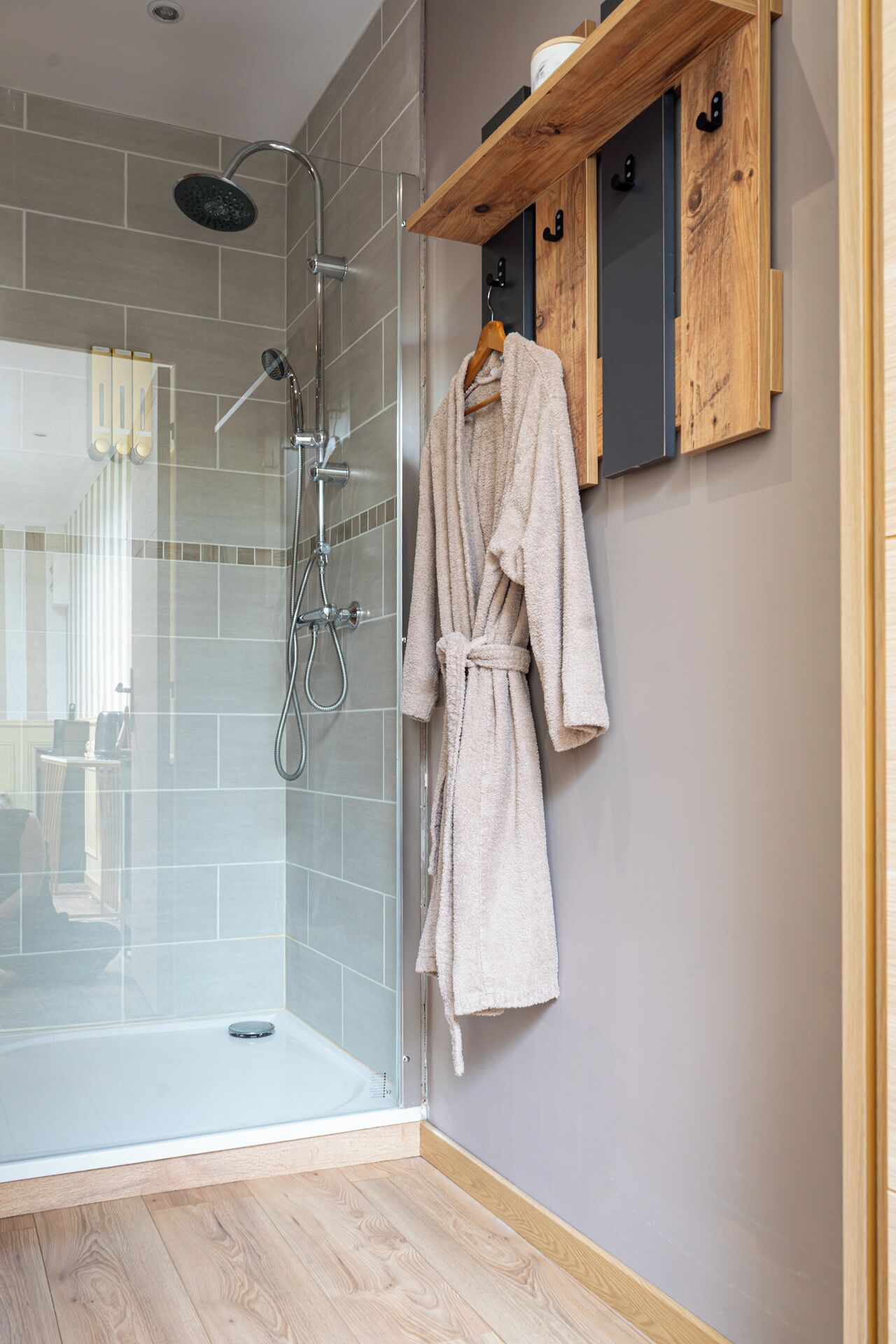 Un baño moderno con cabina de ducha de vidrio, alfombra de baño de madera y una bata colgada en la pared.