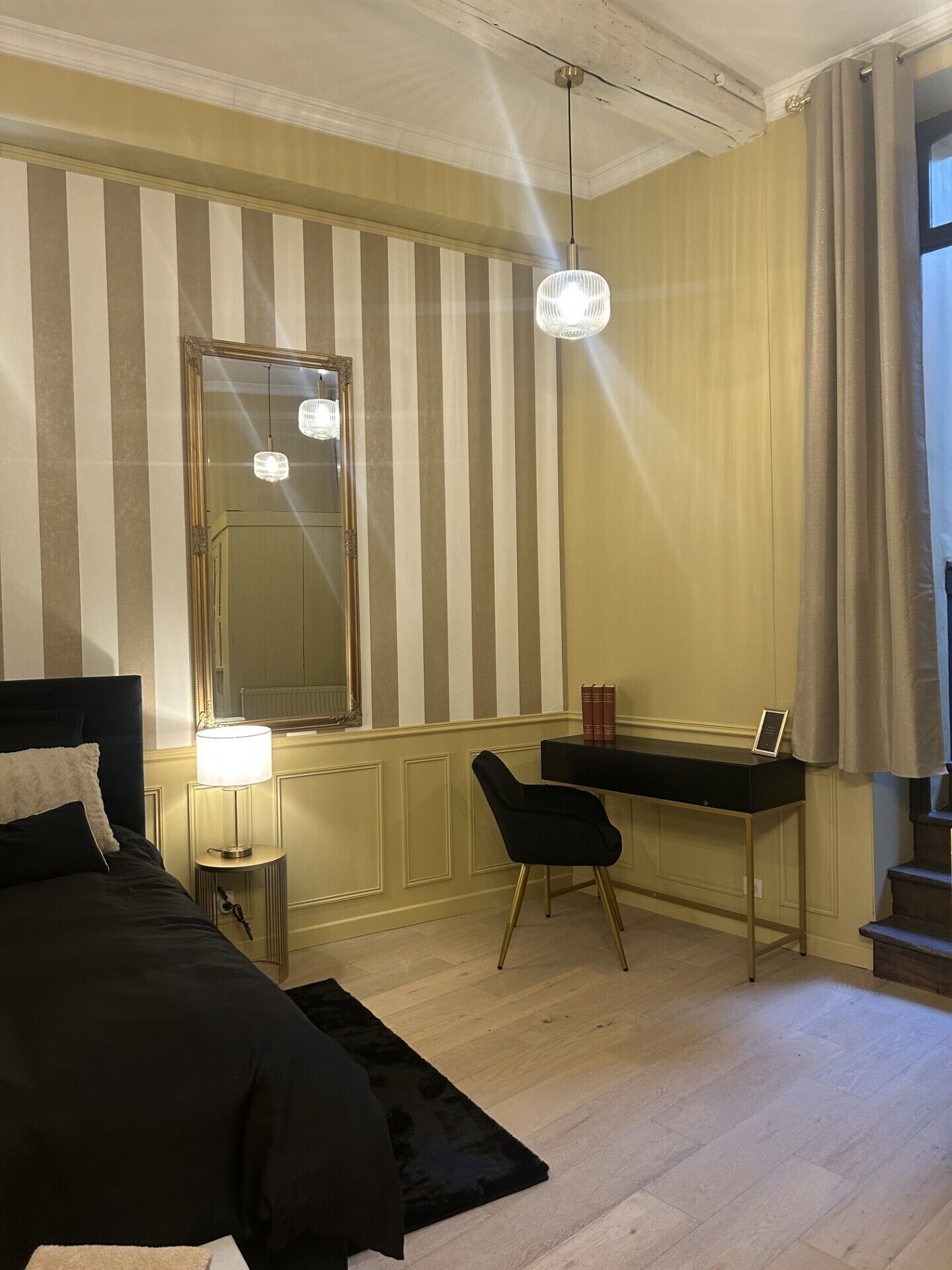 Una habitación de hotel con cama, escritorio, silla, lámpara, espejo y ventana con cortinas.