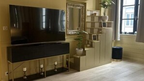 A modern living room with a large flat-screen TV, a decorative mirror, a plant, and a bookshelf. - Imperial Suite & Spa (Béthune)