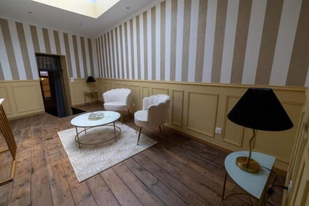 A room with striped wallpaper, a round table with chairs, a lamp, and wooden flooring.