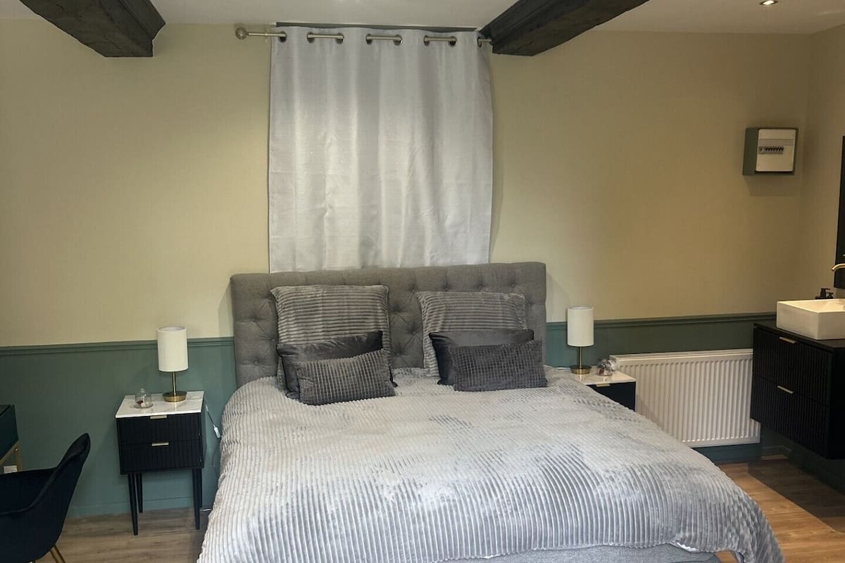 A bedroom with a large bed, two bedside tables, a chair, a radiator, and a mirror.