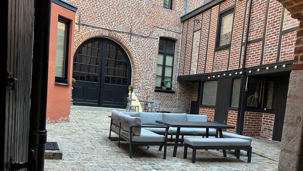 An outdoor courtyard with a brick building, a black gate, and a seating area with a table and chairs. - Imperial Suite & Spa (Béthune)