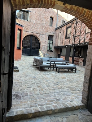 An outdoor courtyard with a brick building, a black gate, and a seating area with a table and chairs. - Imperial Suite & Spa (Béthune)