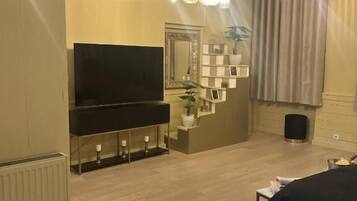 A modern bedroom with a large bed, a TV, a mirror, and a small seating area with a plant.