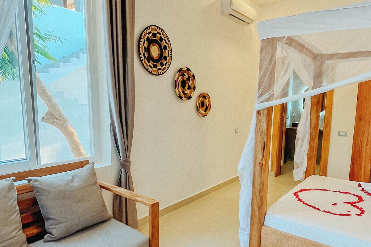 A bedroom with a bed, a sofa, a small table, and a ceiling fan.