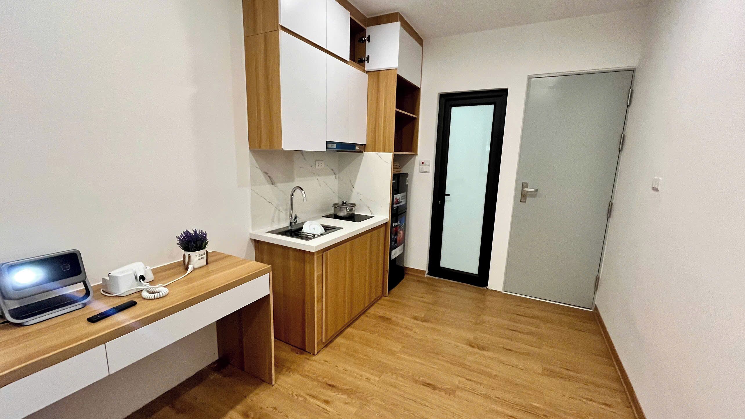 Une cuisine compacte avec un plan de travail en bois, un évier encastré et une petite cuisinière. Une porte donne accès à une autre pièce, et une étagère est fixée au mur au-dessus de l’évier.