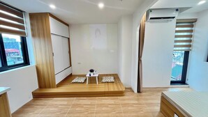 Un dormitorio moderno con una plataforma de madera, una mesita con una planta en maceta y una cama con almohadones estampados.