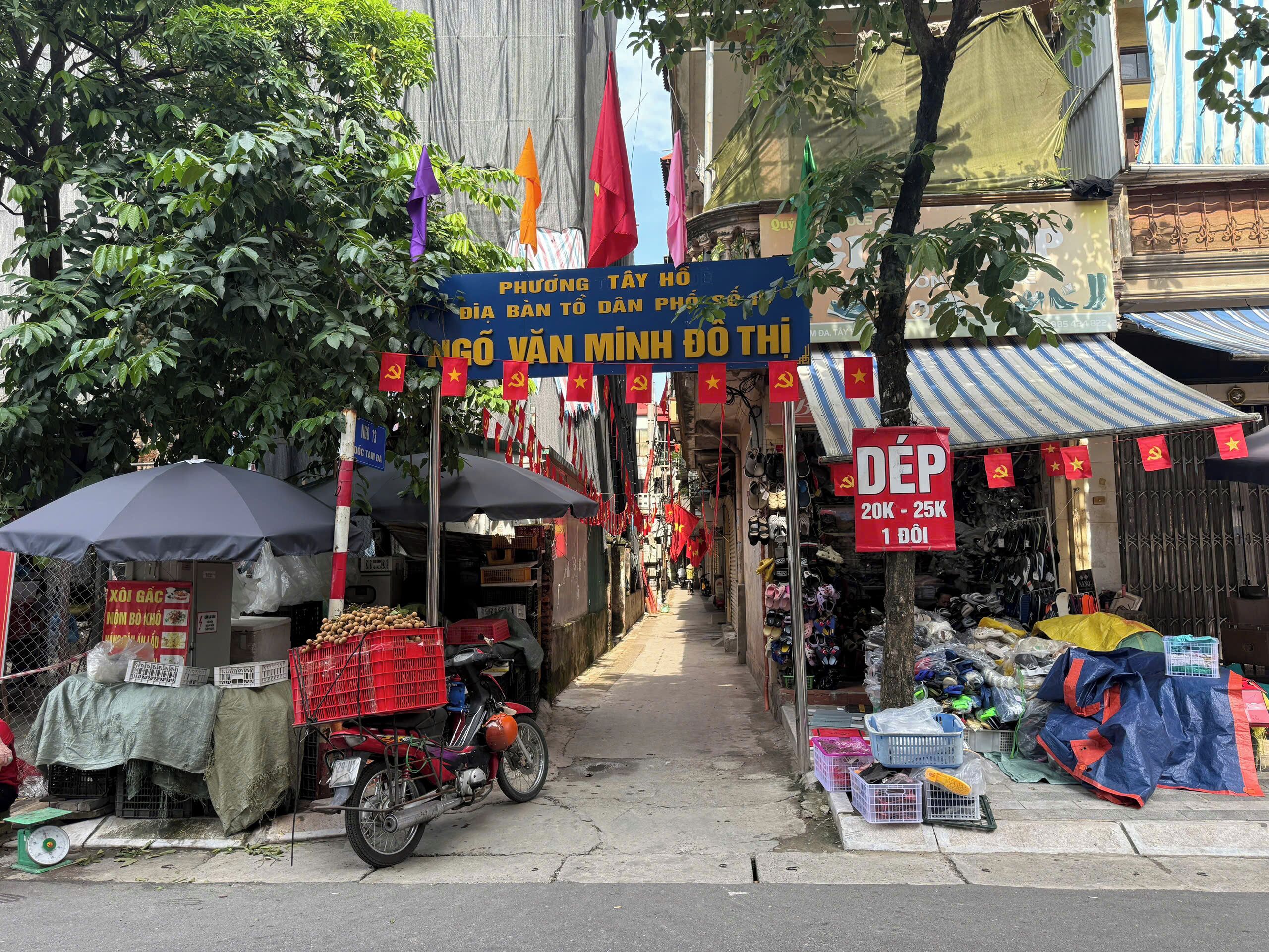 A narrow street with various shops and stalls, some with Vietnamese flags.