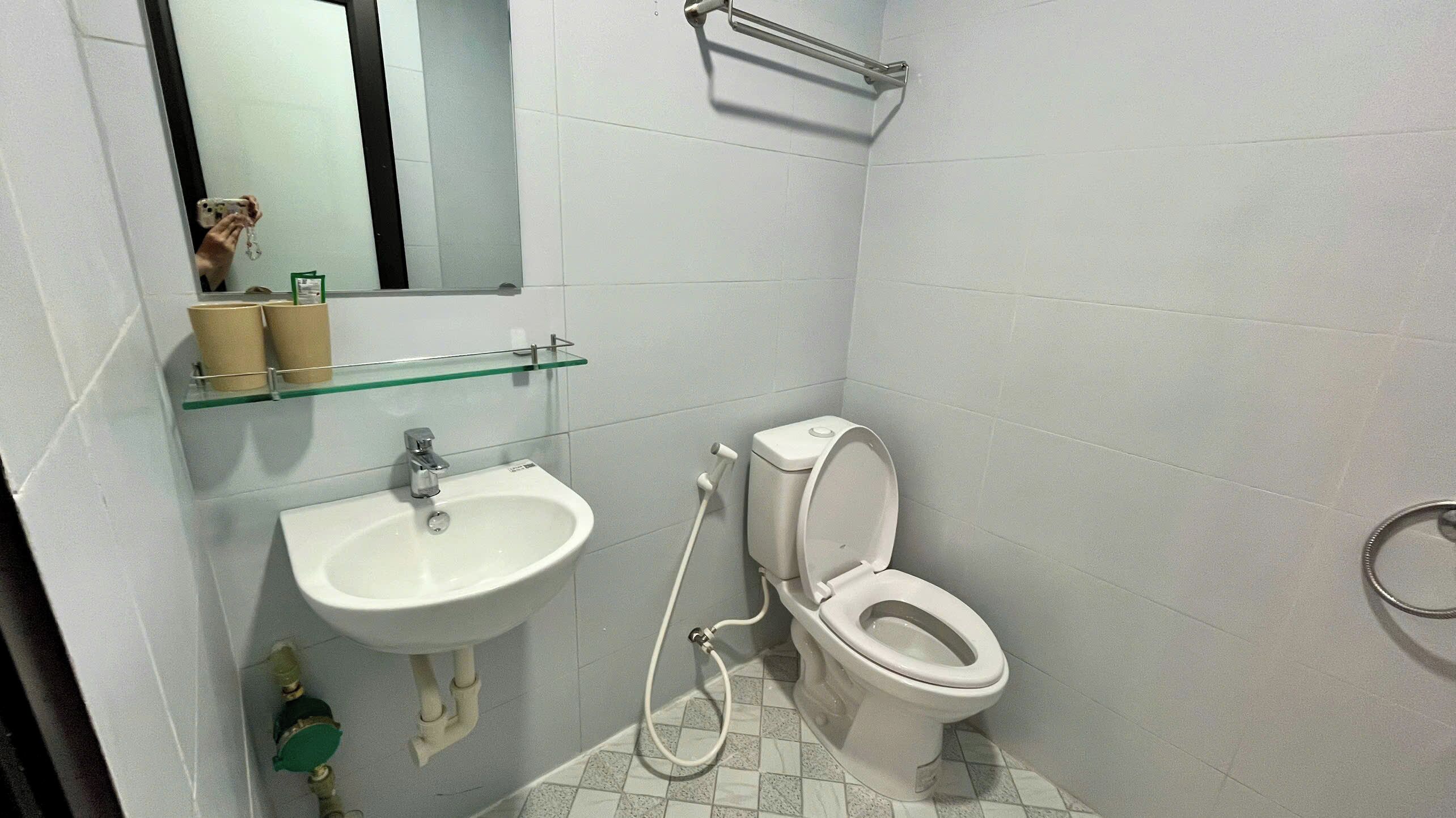 A small bathroom with a white sink, a toilet, and a glass shelf above the sink.