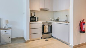 Una cocina compacta con armarios blancos, microondas, horno y cafetera.