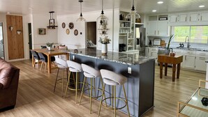 A modern kitchen with a central island, bar stools, and a dining area with a wooden table and chairs. - Lakefront home in Radford with private dock, large deck, and great views (Radford)