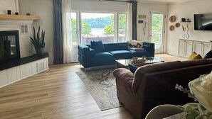 A living room with a blue sofa, a brown sofa, a glass coffee table, and a fireplace. - Lakefront home in Radford with private dock, large deck, and great views (Radford)