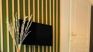 Et værelse med et hvidt bord, en glaskrukke med tørrede planter, et sort fjernsyn på en grøn væg og en grøn stol.