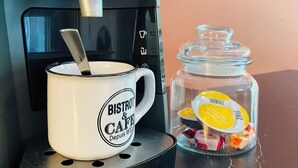 En kaffemaskine, en kop og et glas med sukker på et bord.