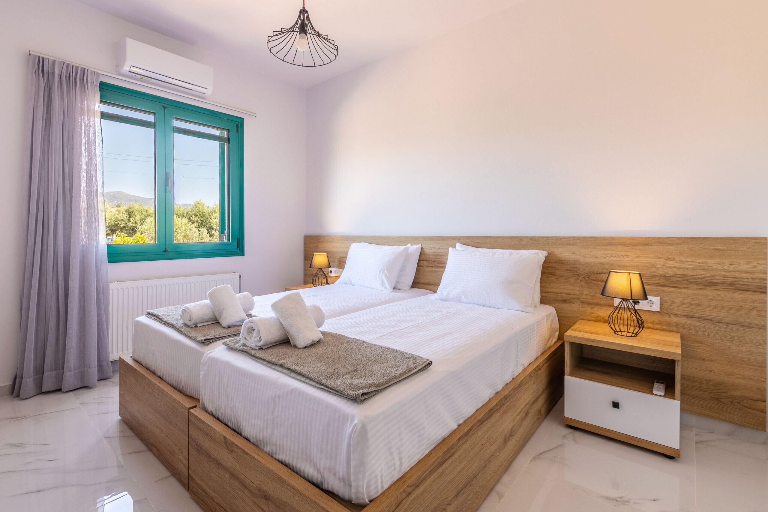 A bedroom with a wooden bed, white bedding, a nightstand with a lamp, and a window with curtains.