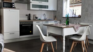 Una cocina moderna con armarios blancos, horno integrado, microondas y estufa. Hay una mesa de comedor con dos sillas blancas y una ventana con vistas al exterior.