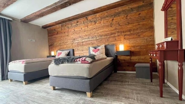 Un dormitorio con dos camas, paneles de madera en la pared y un viguería de madera.