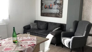 Una sala de estar con una mesa de madera, sillas blancas, un sofá gris y un sillón gris.
