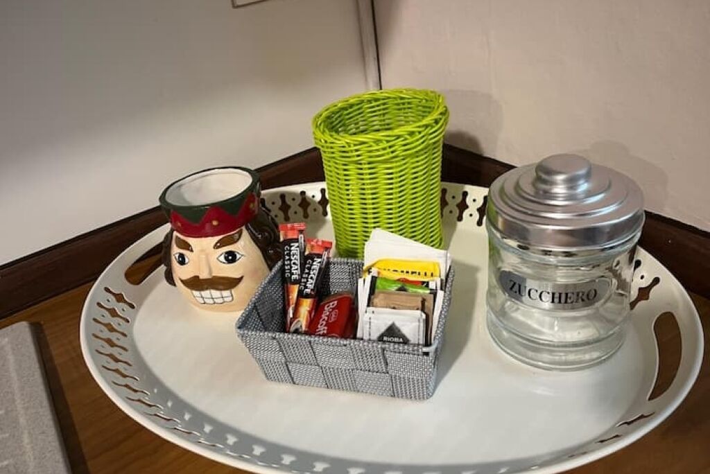 A tray with a decorative mug, a wicker basket, a metal container labeled "ZUCCHERO," and a box of Nespresso Classic coffee capsules.