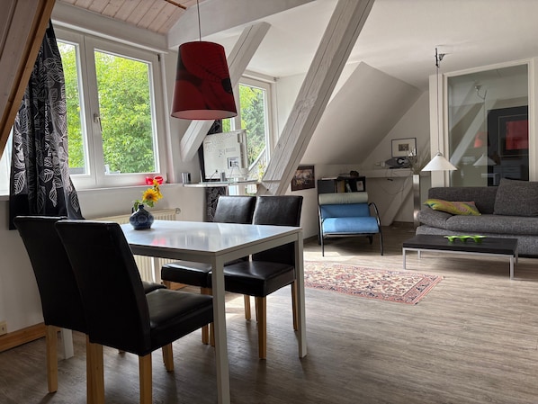 A modern loft-style living space with a dining area, a sofa, and a view of greenery outside.