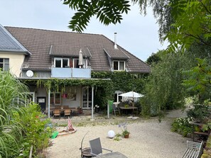 A two-story house with a covered patio area, a gravel yard, and various outdoor furniture.
