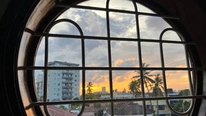 A view through a window with a grid pattern, featuring a sunset and buildings in the background.