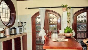 A kitchen with wooden cabinets, a wooden countertop, a microwave, a kettle, and a window with curtains.