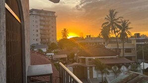 A sunset view from a balcony overlooking a residential area with buildings and palm trees.