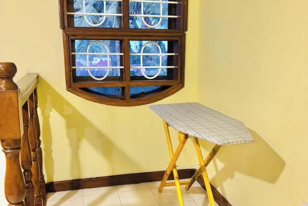 Una stanza angolare con una scala in legno, un tavolino con tovaglia a scacchi e una finestra vista alberi.