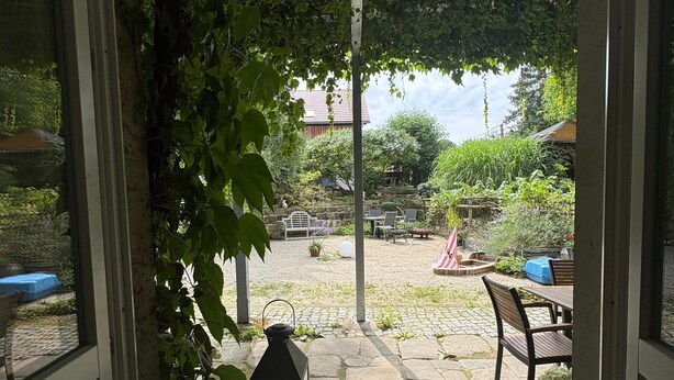 Une vue à travers une porte donnant sur une cour intérieure, avec un sol en pierre, une lanterne et du mobilier d’extérieur.
