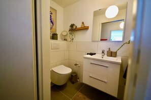 Een badkamer met toilet, wastafel, spiegel en een plank met planten.