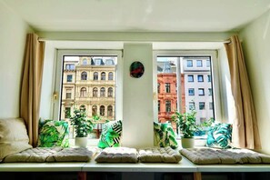 A room with a window seat, potted plants, and a view of historic buildings.