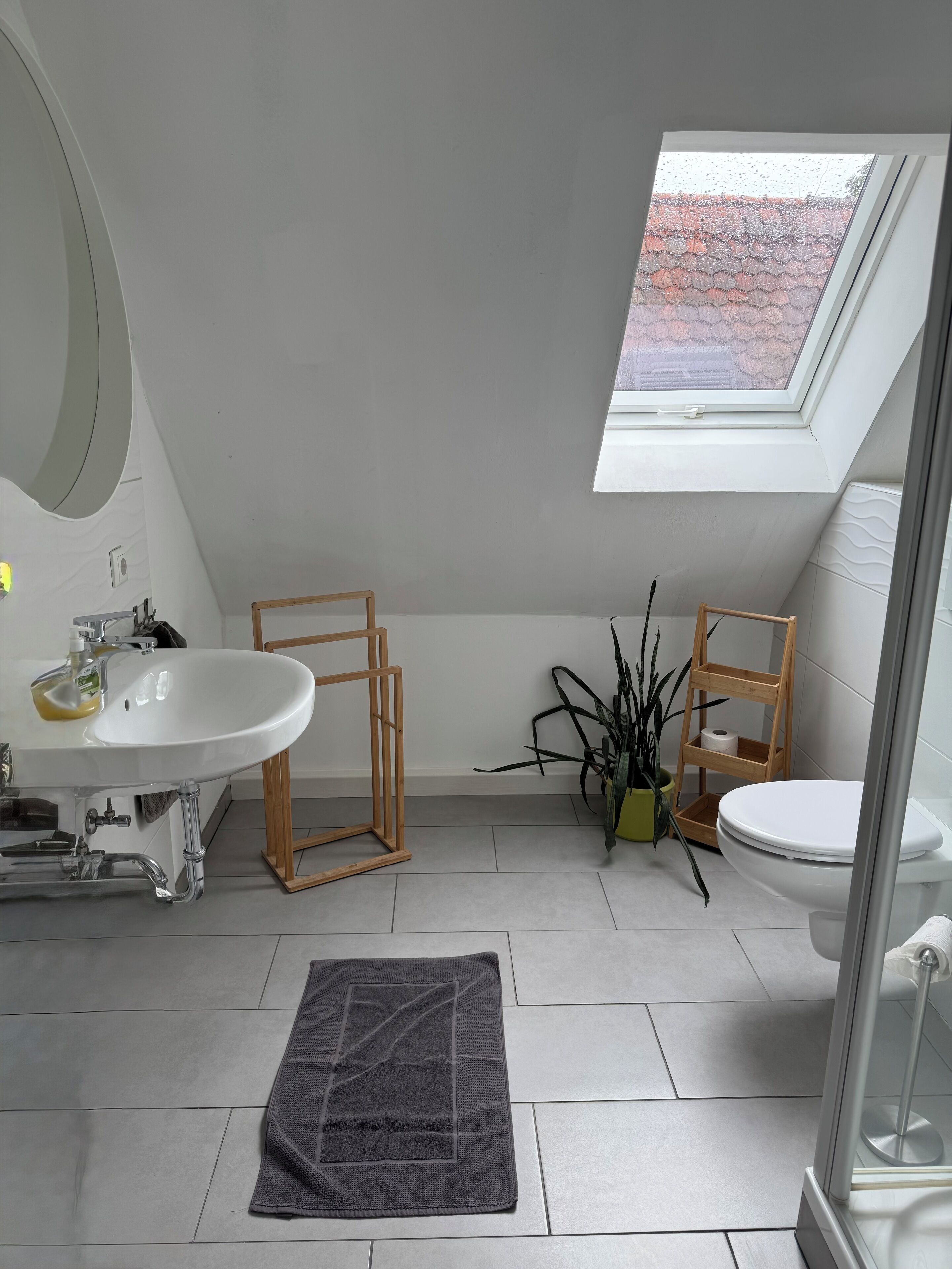 A modern bathroom with a skylight, a white sink, a toilet, and a shower area.