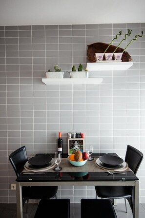 A dining area with a table set for four, a wine bottle, and a bowl of fruit.