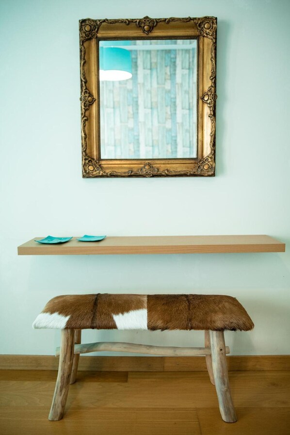 A wooden bench with a fur seat, a wooden shelf with two blue plates, and a mirror with an ornate gold frame.