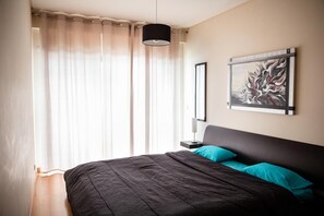 A bedroom with a bed, curtains, a painting, and a nightstand.