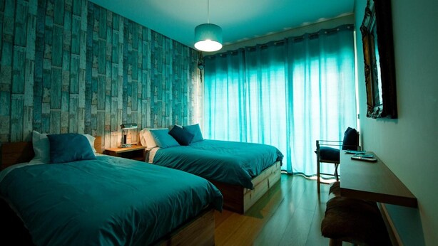 Une chambre avec deux lits, un bureau, une lampe et une fenêtre avec des rideaux.